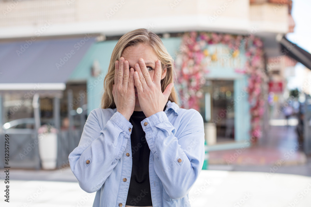 pretty woman covering face with hands, peeking between fingers with surprised expression and looking to the side pretty woman covering face with hands, peeking between fingers with surprised expression and looking to the side