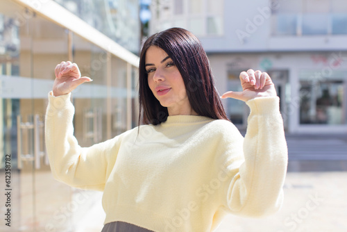 young pretty woman feeling proud, arrogant and confident, looking satisfied and successful, pointing to self