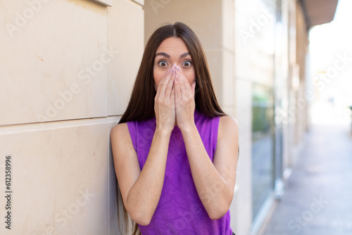 young pretty woman looking happy, cheerful, lucky and surprised covering mouth with both hands