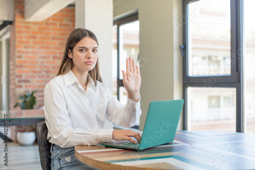 young pretty woman looking serious showing open palm making stop gesture. working with a laptop