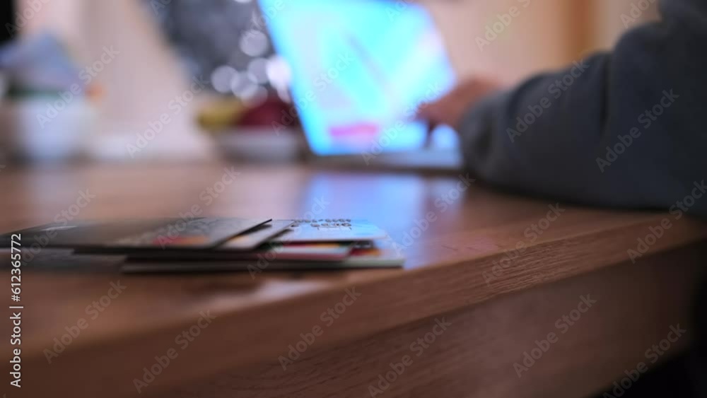 Stack of different bank cards lying on wooden table and in blurred background with working person at laptop. Efficient money management. Work from home. Stack of different bank cards lying on wooden table and in blurred background with working person at laptop. Efficient money management. Work from home.