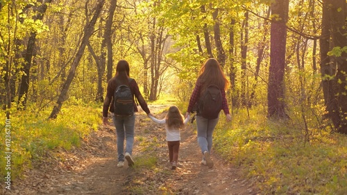 Young travel girl are walking with small child sunset through forest park. Traveler girls go along path forest tourist backpacks. happy holiday weekend spent with family. happy family life concept