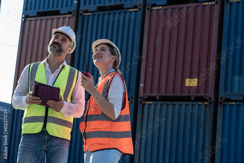 Foreman holding file discussing with female worker wearing safety helmet and helping to inspect container loading in container yard