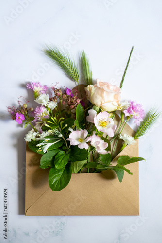 Various flowers in an open craft mail envelope on a marble pastel background. Flat lay. Minimalistic composition. Concept of love and nature