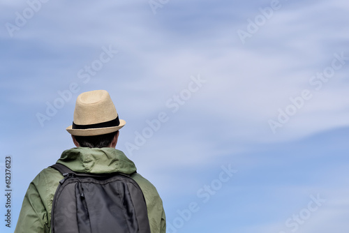 Back view of a traveler man with a backpack against the blue sky with copy space.Tourist, backpacker in a hat looks at the sky.