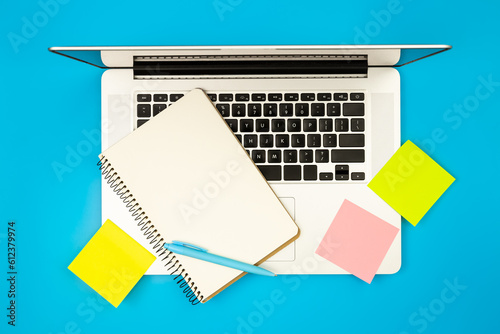 Laptop  notepad and paper reminders on blue background  flat lay.