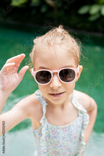Happy child in sunglasses in the swimming pool. Funny kid playing outdoors in jungle resort. Summer vacation concept
