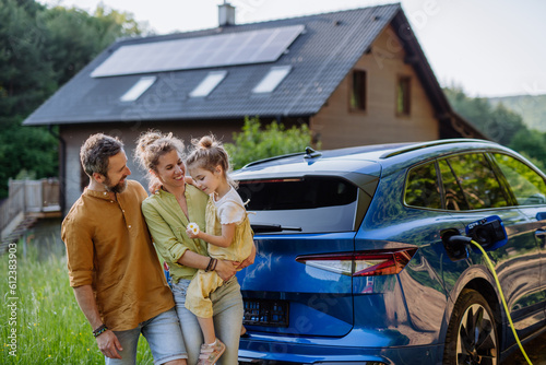 Foto Family with little girl standing in front of their house with solar panels on the roof, having electric car