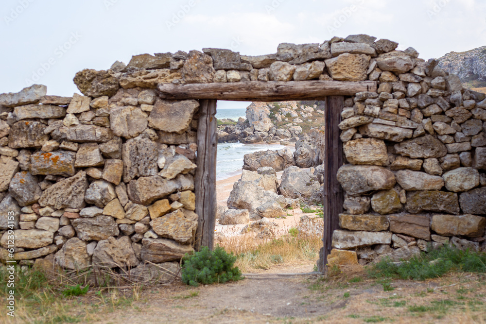 An old dilapidated stone wall with a doorway overlooking the sea and the rocky shore. Film decoration