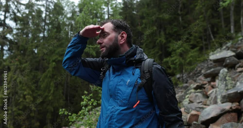 A male tourist with a backpack is standing on large stones. A close-up tourist looks at the landscape in rainy weather. Backpack walking in the mountains on stones in the rain. A male tourist with a backpack is standing on large stones. A close-up tourist looks at the landscape in rainy weather. Backpack walking in the mountains on stones in the rain.