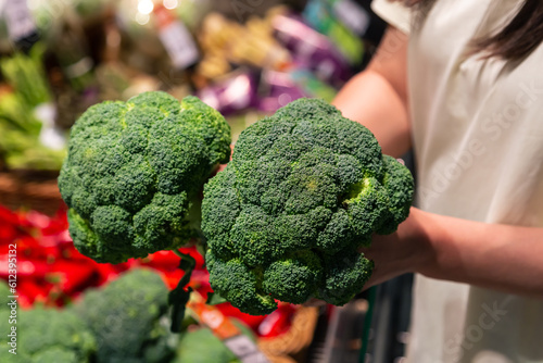 The woman holds broccoli in the store or in the market, close up.