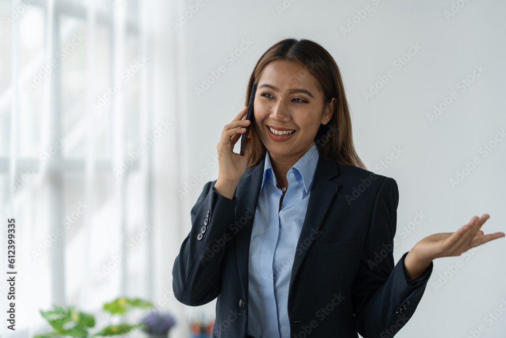 Happy Asian businesswoman talking on the phone and smiling while sitting at work using smartphone to talk. Contact via online application, concept of management Happy Asian businesswoman talking on the phone and smiling while sitting at work using smartphone to talk. Contact via online application, concept of management