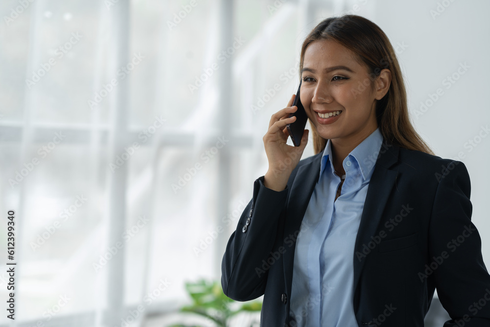 Happy Asian businesswoman talking on the phone and smiling while sitting at work using smartphone to talk. Contact via online application, concept of management Happy Asian businesswoman talking on the phone and smiling while sitting at work using smartphone to talk. Contact via online application, concept of management
