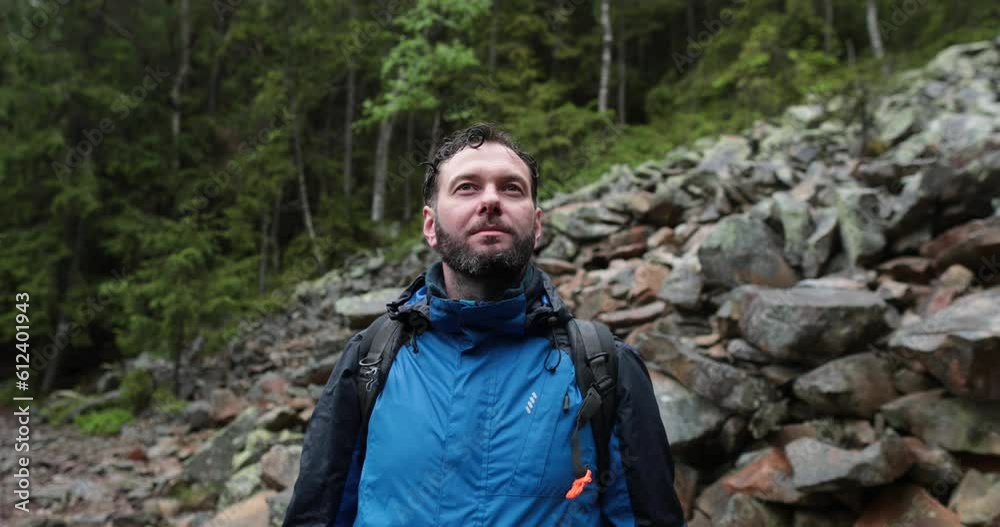 A male tourist with a backpack is standing on large stones. A close-up tourist looks at the landscape in rainy weather. Backpack walking in the mountains on stones in the rain. A male tourist with a backpack is standing on large stones. A close-up tourist looks at the landscape in rainy weather. Backpack walking in the mountains on stones in the rain.