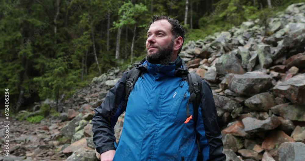A male tourist with a backpack is standing on large stones. A close-up tourist looks at the landscape in rainy weather. Backpack walking in the mountains on stones in the rain. A male tourist with a backpack is standing on large stones. A close-up tourist looks at the landscape in rainy weather. Backpack walking in the mountains on stones in the rain.