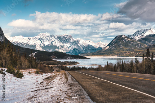 View of highway road into the rocky mountains and frozen lake in Icefields Parkway