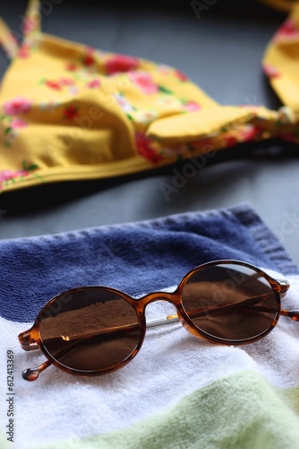 Yellow floral bikini, straw hat, striped towel and sunglasses on dark background. Selective focus.