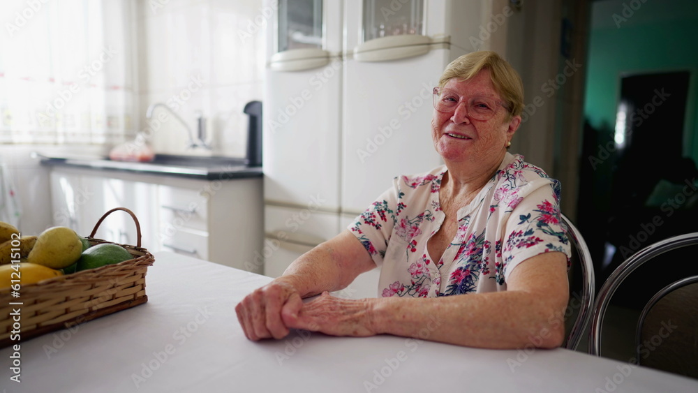 Happy senior woman smiling at camera in authentic domestic lifestyle. A caucasian elderly person in 80s smiling at camera while sititng at kitchen Happy senior woman smiling at camera in authentic domestic lifestyle. A caucasian elderly person in 80s smiling at camera while sititng at kitchen