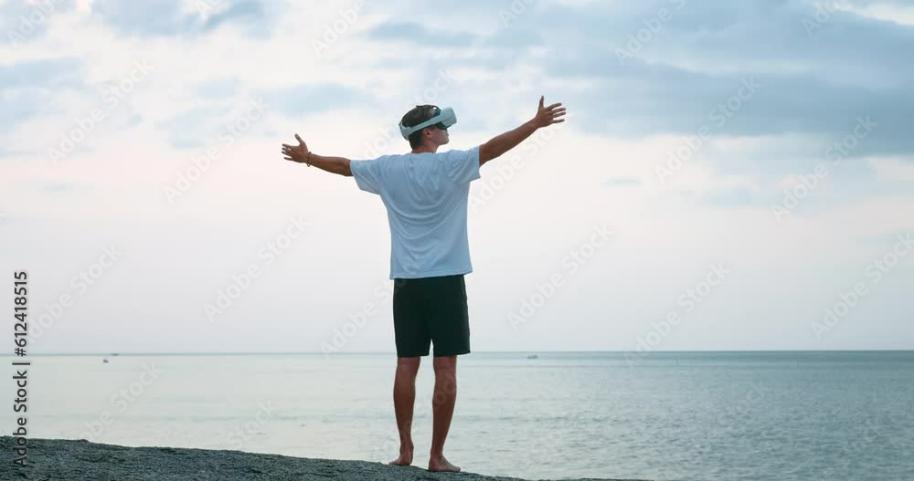 Young man in virtual reality glasses at sunset, raises his hands in the air, spins, rejoicing at the sunset on the sea, in augmented reality using Virtual Reality Headset. Virtual summer vacation Young man in virtual reality glasses at sunset, raises his hands in the air, spins, rejoicing at the sunset on the sea, in augmented reality using Virtual Reality Headset. Virtual summer vacation