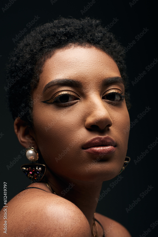 Close up view of young and short haired african american woman with earrings and evening makeup looking at camera isolated on black with lighting, high fashion and evening look Close up view of young and short haired african american woman with earrings and evening makeup looking at camera isolated on black with lighting, high fashion and evening look