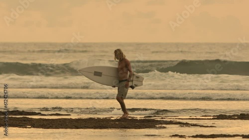 Cinematic tired exhausted drained jaded caucasian man bodyboarder goes after bodyboarding workout from big epic ocean waves. Concept fatigue after sports workout, exhaustion after bodyboarding session photo