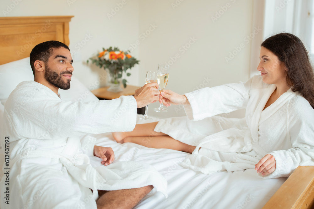 © Prostock-studio - Newlywed Couple Clinking Glasses Enjoying Sparkling Wine In Hotel Bedroom