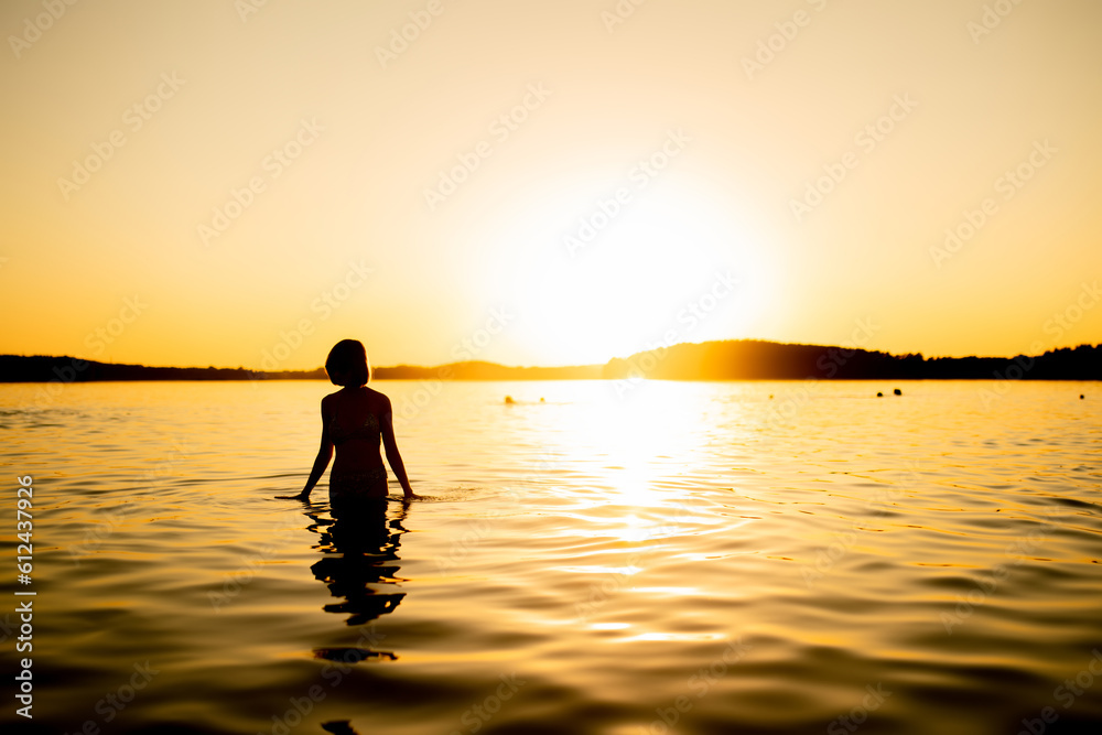 Silhouette of beautiful teenage girl having fun by a lake on warm and sunny summer evening. Pretty young girl on a sunset.