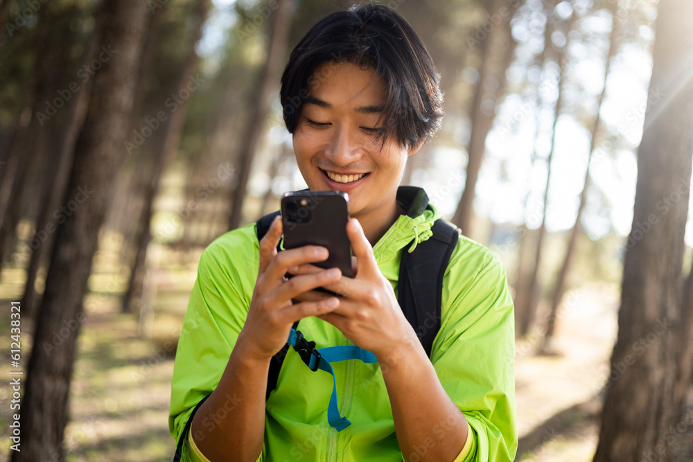A young Korean man is hiking up the mountain while chatting on his mobile phone. Concept of coverage in the field, use the mobile in the mountains, send messages from afar.