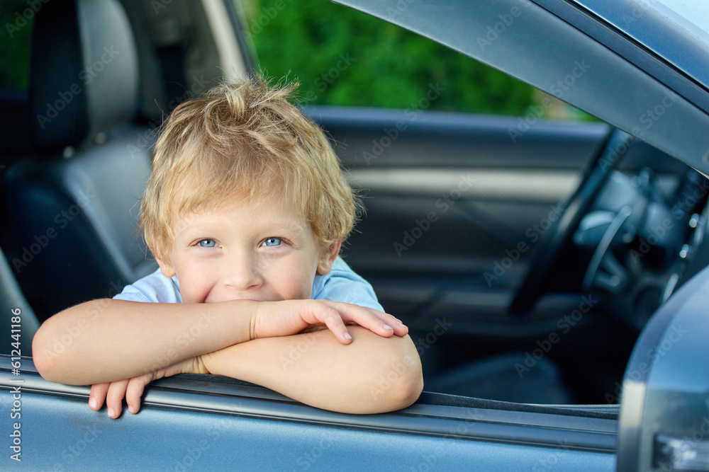 Funny boy is sitting in the car in the passenger seat waiting for the upcoming trip. Small child rides as a passenger in a car, leaning out of an open window Funny boy is sitting in the car in the passenger seat waiting for the upcoming trip. Small child rides as a passenger in a car, leaning out of an open window