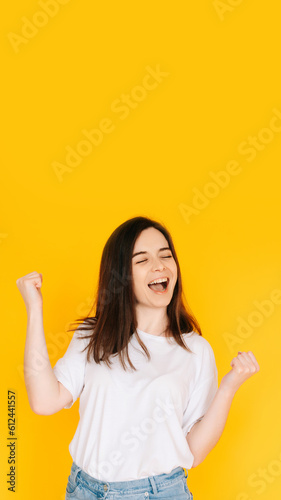 Bilde på lerret Exultant Woman Celebrating with Fist Raised, Shouting 'Yes' - Victory, Achievement, Success Concept on Vibrant Yellow Background