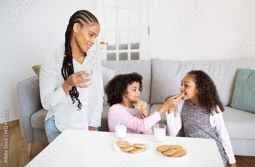 Black Mommy Looking At Daughters Having Fun Eating Cookies Indoors