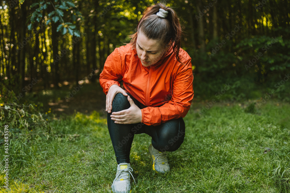 Sad caucasian woman is holding her knee joint in excruciating pain at uphill road. Adventure