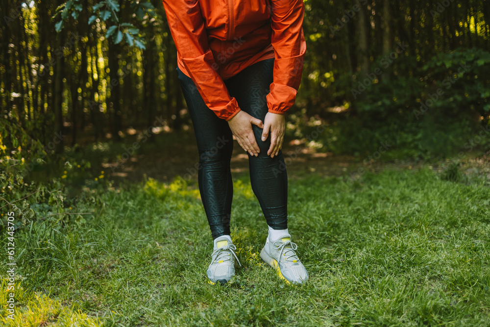 Sad caucasian woman is holding her knee joint in excruciating pain at uphill road. Adventure