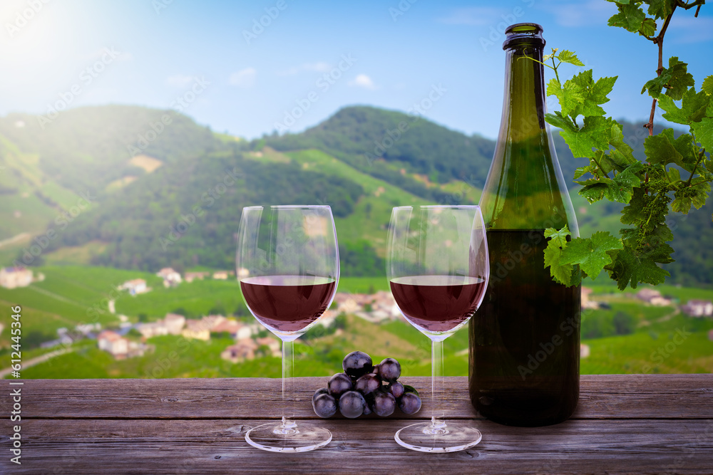 bottle of wine and glasses of red wine, on a wooden table and italian vineyards in the background