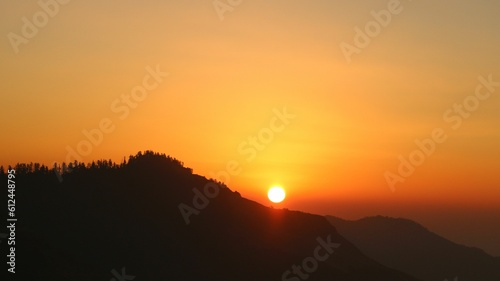 Beautiful sunset in front of the mountains with an orange sky in the background © Taguas Dhyay/Wirestock Creators