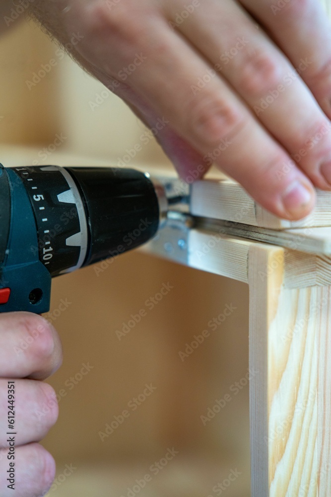 Vertical shot of a man repairing a wooden table with a drill on the blurred background