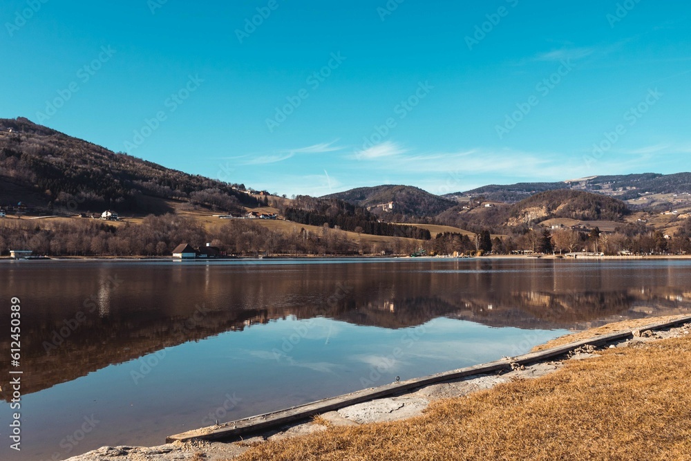 Hill with houses reflected on the water of a lake under a blue sky