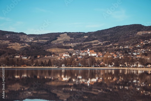 Fototapeta Naklejka Na Ścianę i Meble -  Hill with houses reflected on the water of a lake under a blue sky