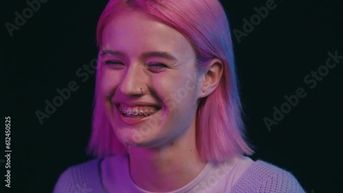 Cheerful young woman with braces smiling sincerely on black background, mood
