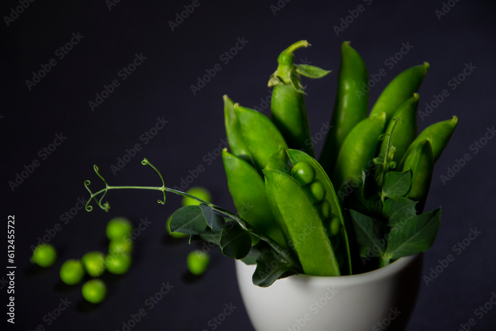 Vertical bunch of green peas in a cup on a black background
