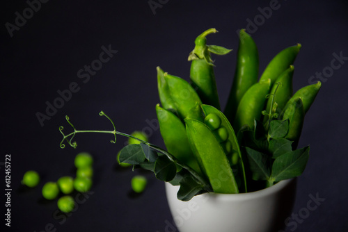 Obraz na płótnie Vertical bunch of green peas in a cup on a black background w salonie