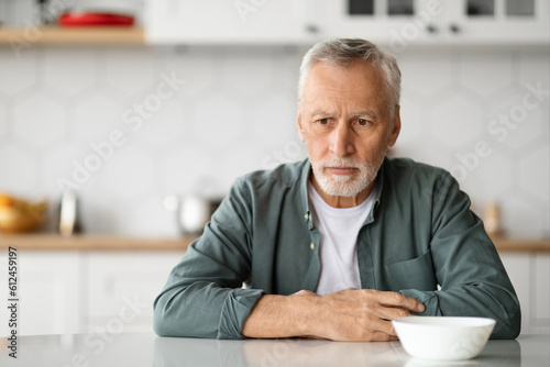 Depression In Seniors. Upset Elderly Man Sitting At Table In Kitchen