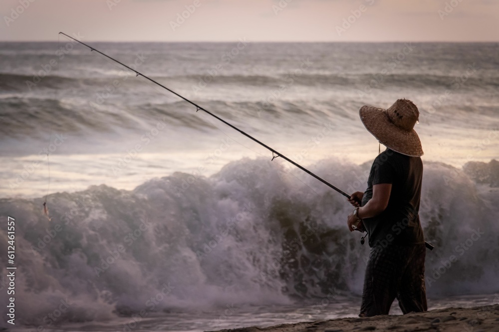 Fisherman standing on the beach with big waves at sunset