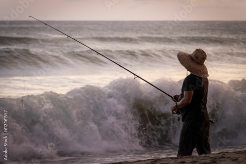 Fisherman standing on the beach with big waves at sunset © Fabien Mazas/Wirestock Creators