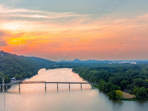 Aerial shot of a bridge on a river surrounded by trees during scenic sunset