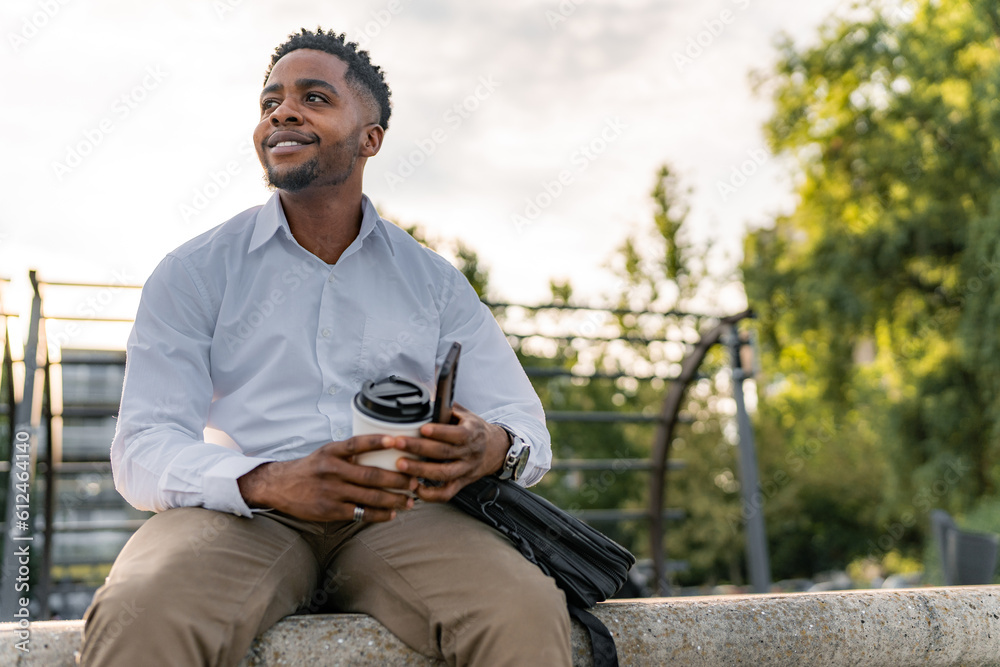 Obraz premium After a hard day at work, a young businessman, elegantly dressed, sits on the promenade, holding a cup of coffee and a mobile phone. With a relaxed demeanor, he takes a moment to relax.