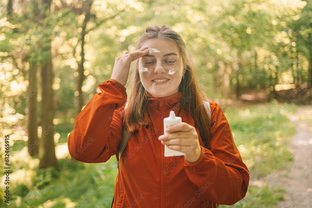 Young woman in a orange sport clothes applying sunscreen lotion while traveling in the mountains. High quality photo