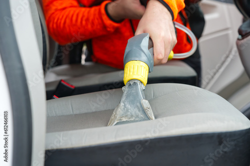 Handyman vacuuming car front textile seat with vacuum cleaner. man cleaning work Minivan.