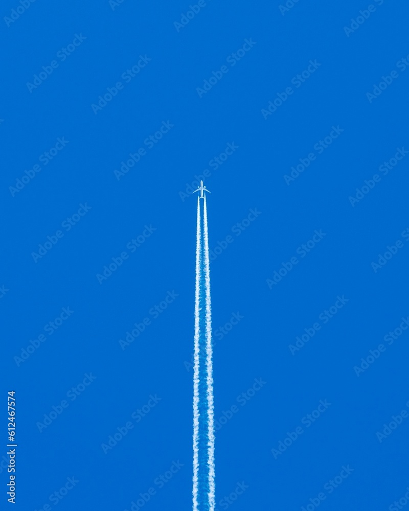 Vertical shot of an airplane flying in blue sky leaving smoke on its trace Vertical shot of an airplane flying in blue sky leaving smoke on its trace