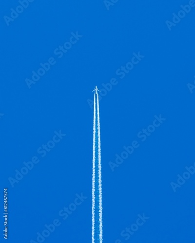 Vertical shot of an airplane flying in blue sky leaving smoke on its trace